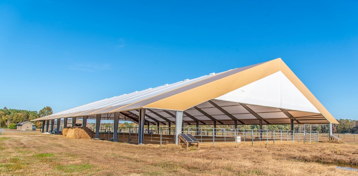 A wide arena building with durable fabric walls stands in the background while a seahorse run is showcased in the foreground, highlighting space and functionality for equestrian use